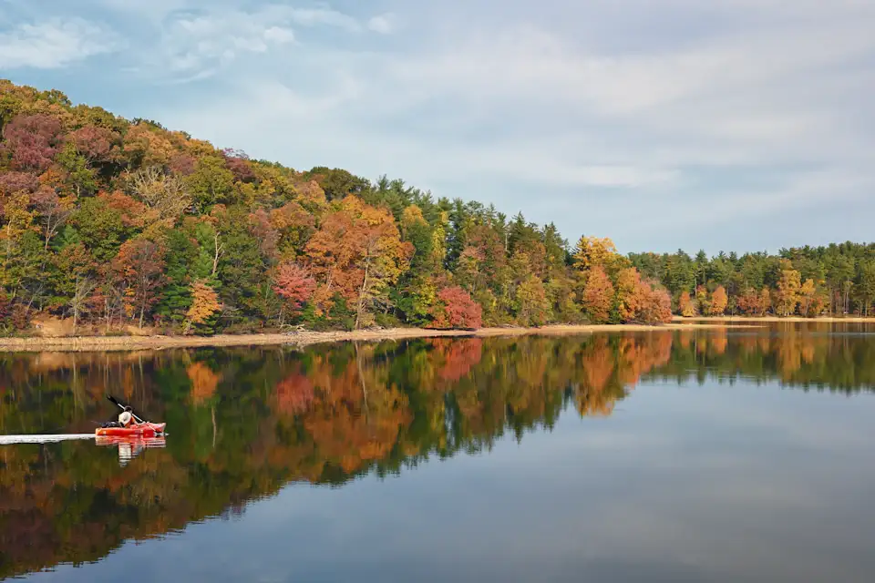 Autumn foliage reflecting on a calm Pocono Mountains lake with a red canoe